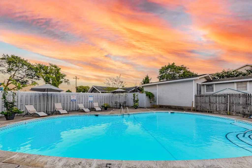 Una piscina junto a un patio cercado bajo un cielo colorido al atardecer.