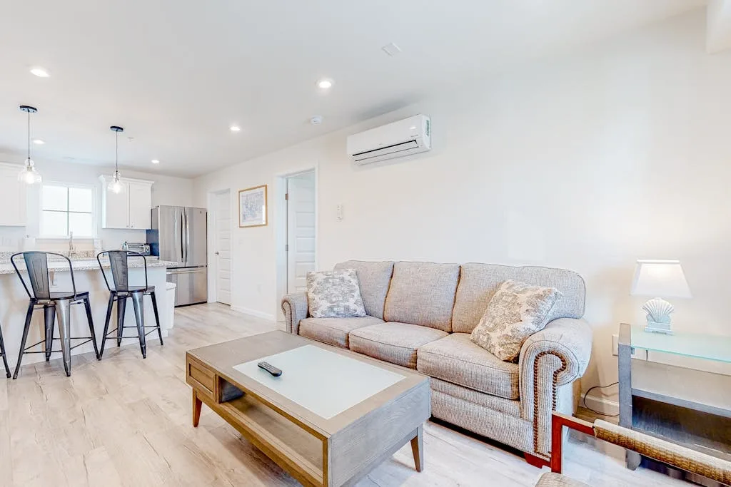 A bright living room with seating and an open kitchen in the background.