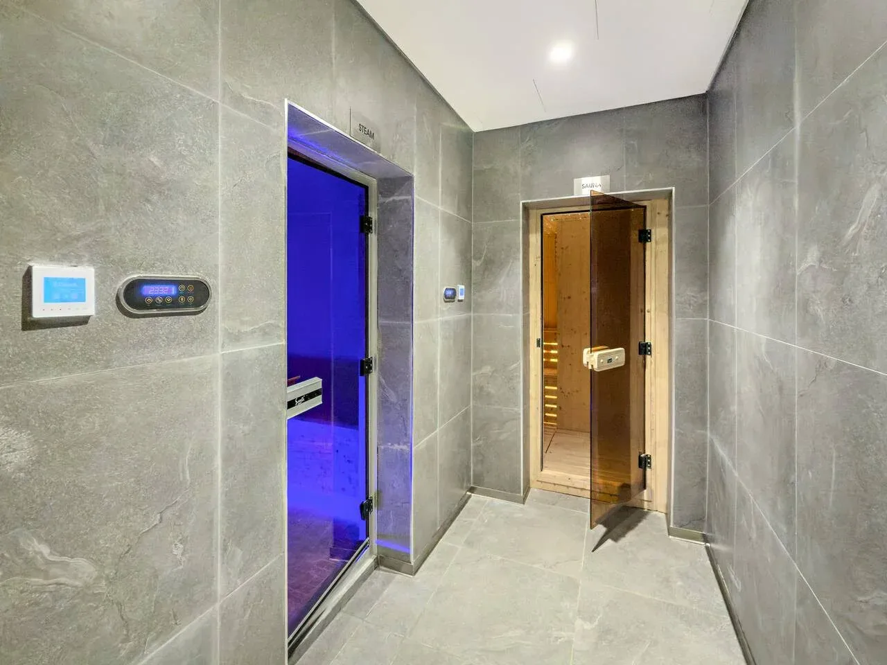 A tiled spa corridor with an open wooden sauna door and a blue-lit room.