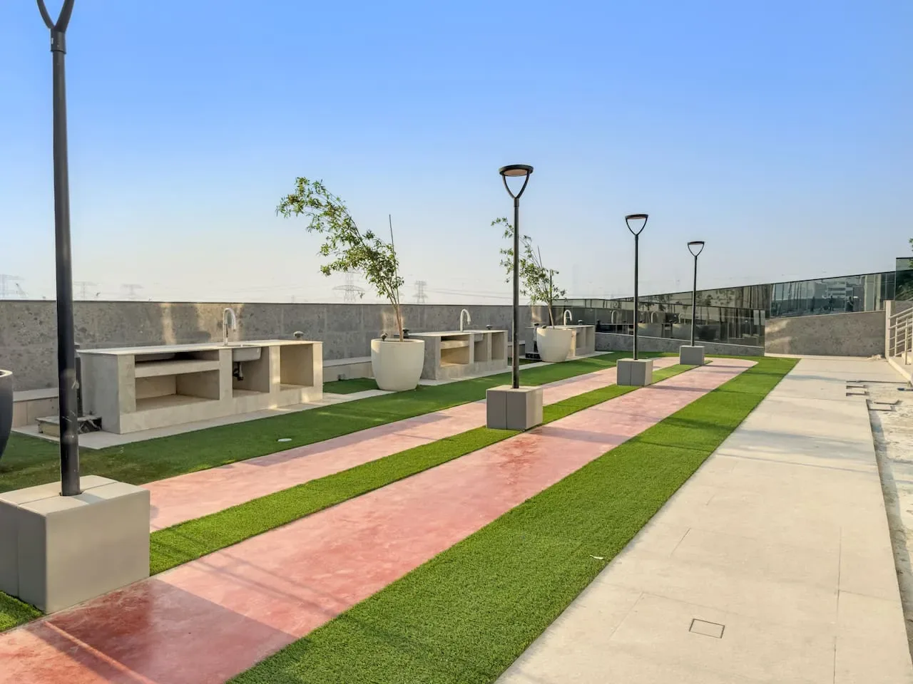 An outdoor terrace has parallel pink walkways, green strips, and built-in counters.