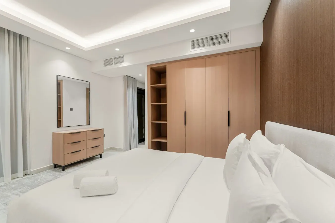 A bright bedroom with a large bed and built-in wooden storage.