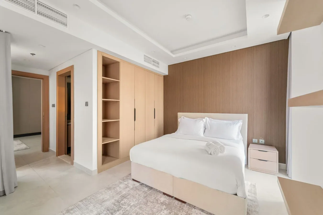 A bright bedroom with a neatly made bed and built-in shelving.