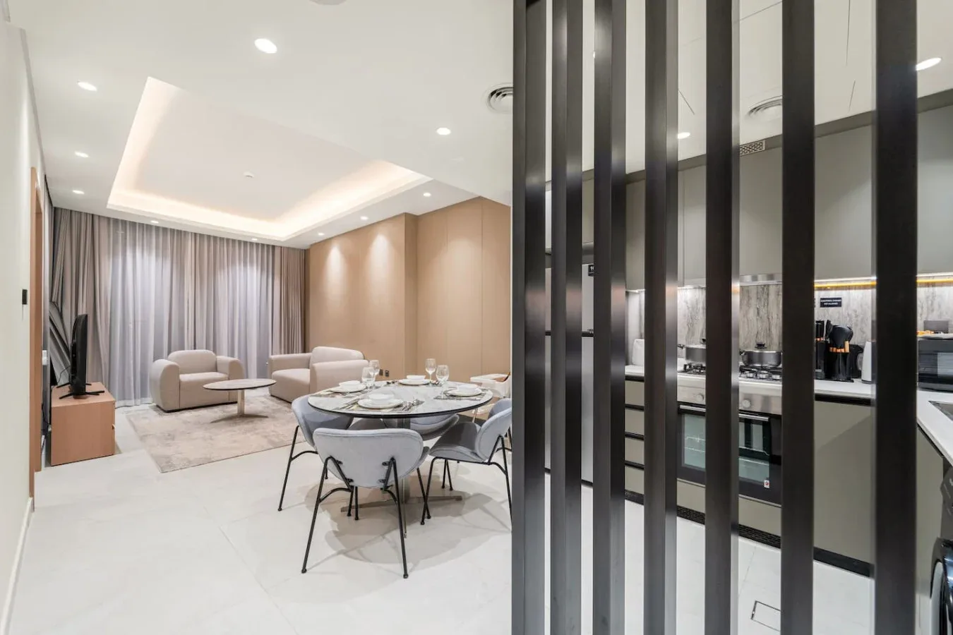 A bright open-plan living and dining area with a kitchen behind dark vertical screens.