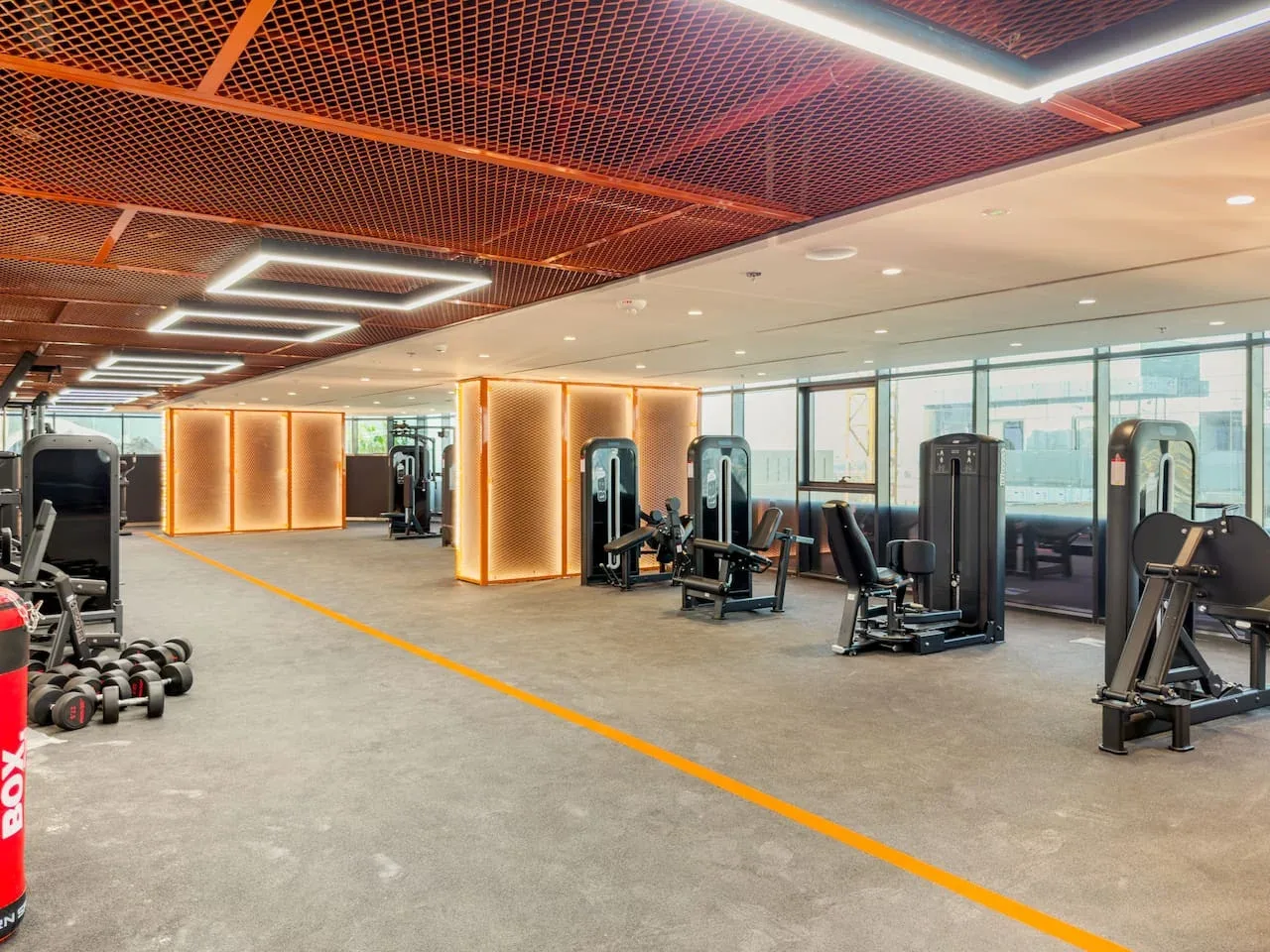A gym with weight machines and dumbbells arranged across an open workout area.