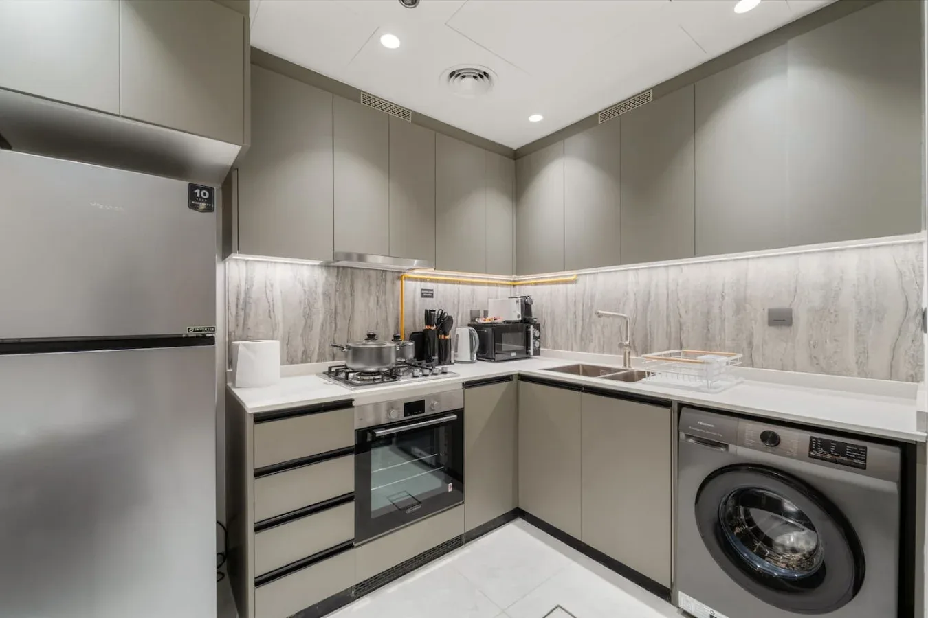 A modern kitchen with white countertops, an oven, and a washing machine.