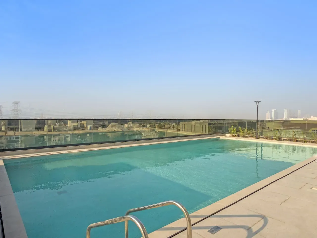 Una piscina en la azotea con una barandilla de vidrio y cielo abierto.