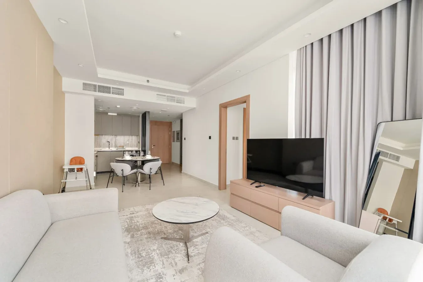 A bright living room with seating, a television, and an open dining area.