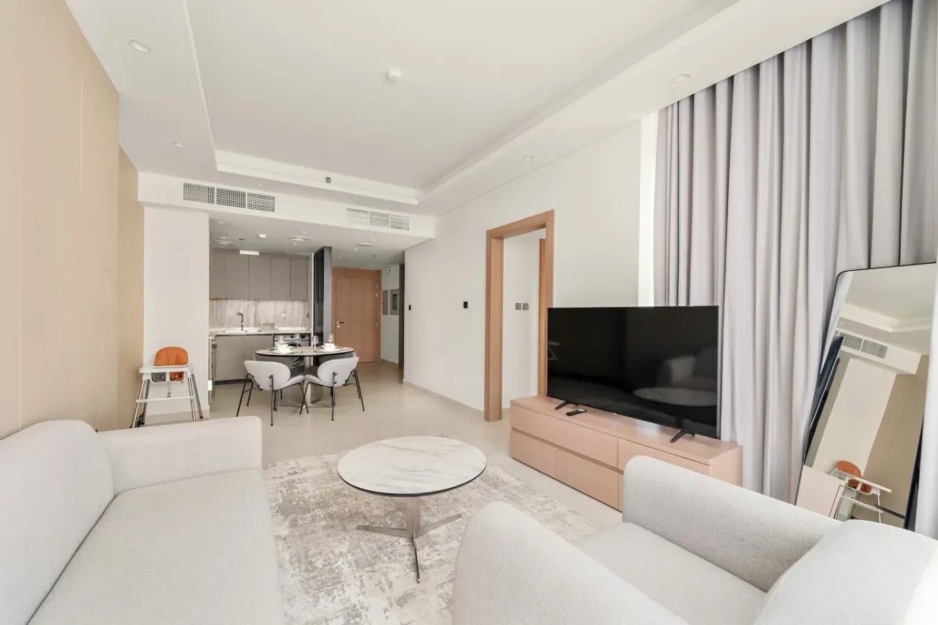 A bright living room with seating, a television, and an open kitchen area.