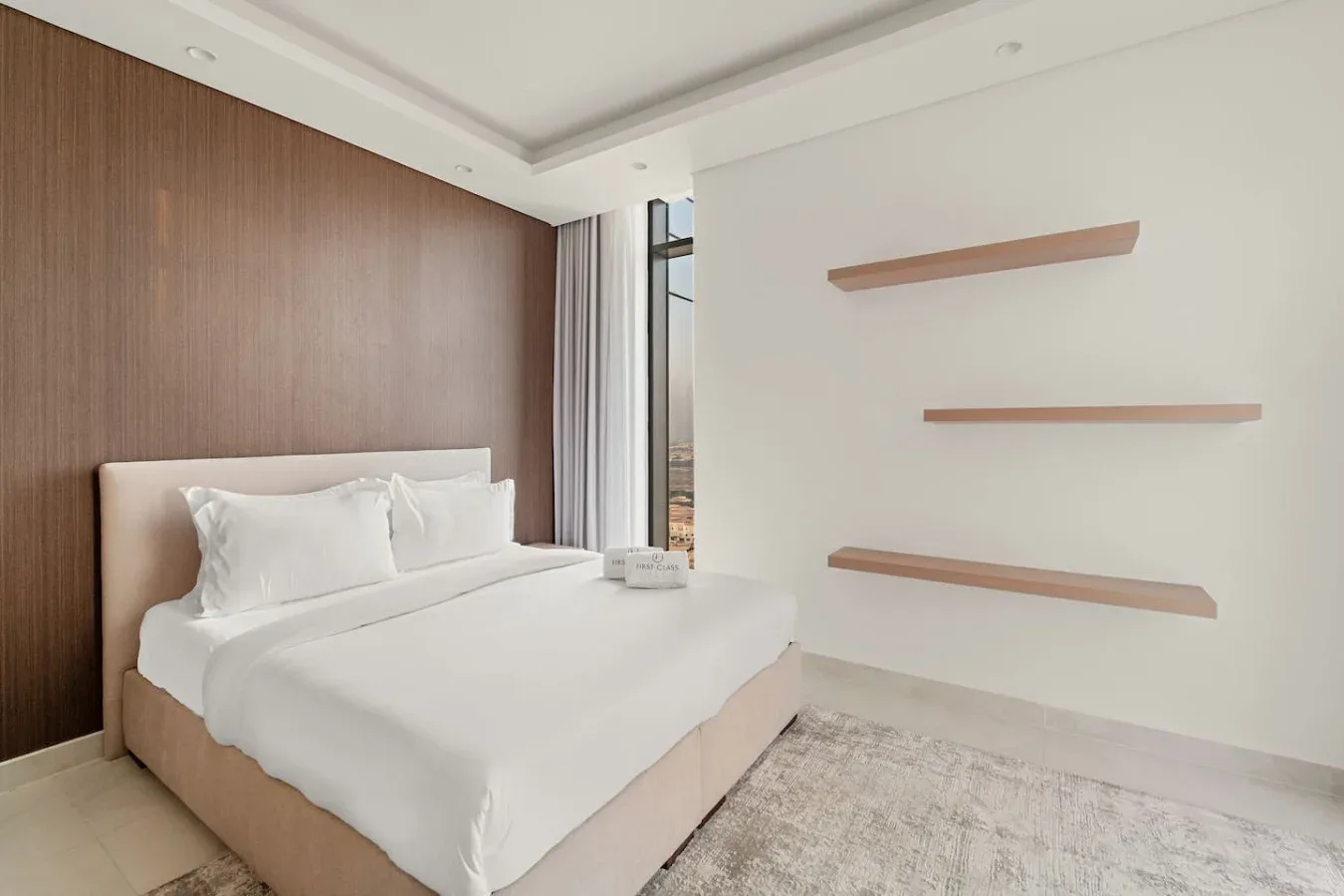 A bedroom with a white bed beside a wall with floating shelves.