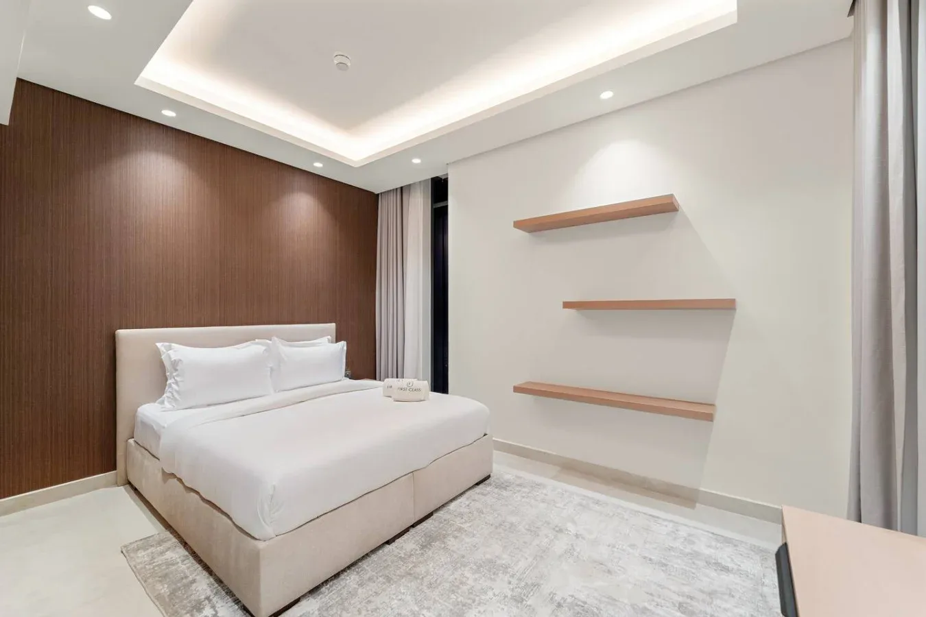 A bright bedroom with a neatly made bed and floating wall shelves.