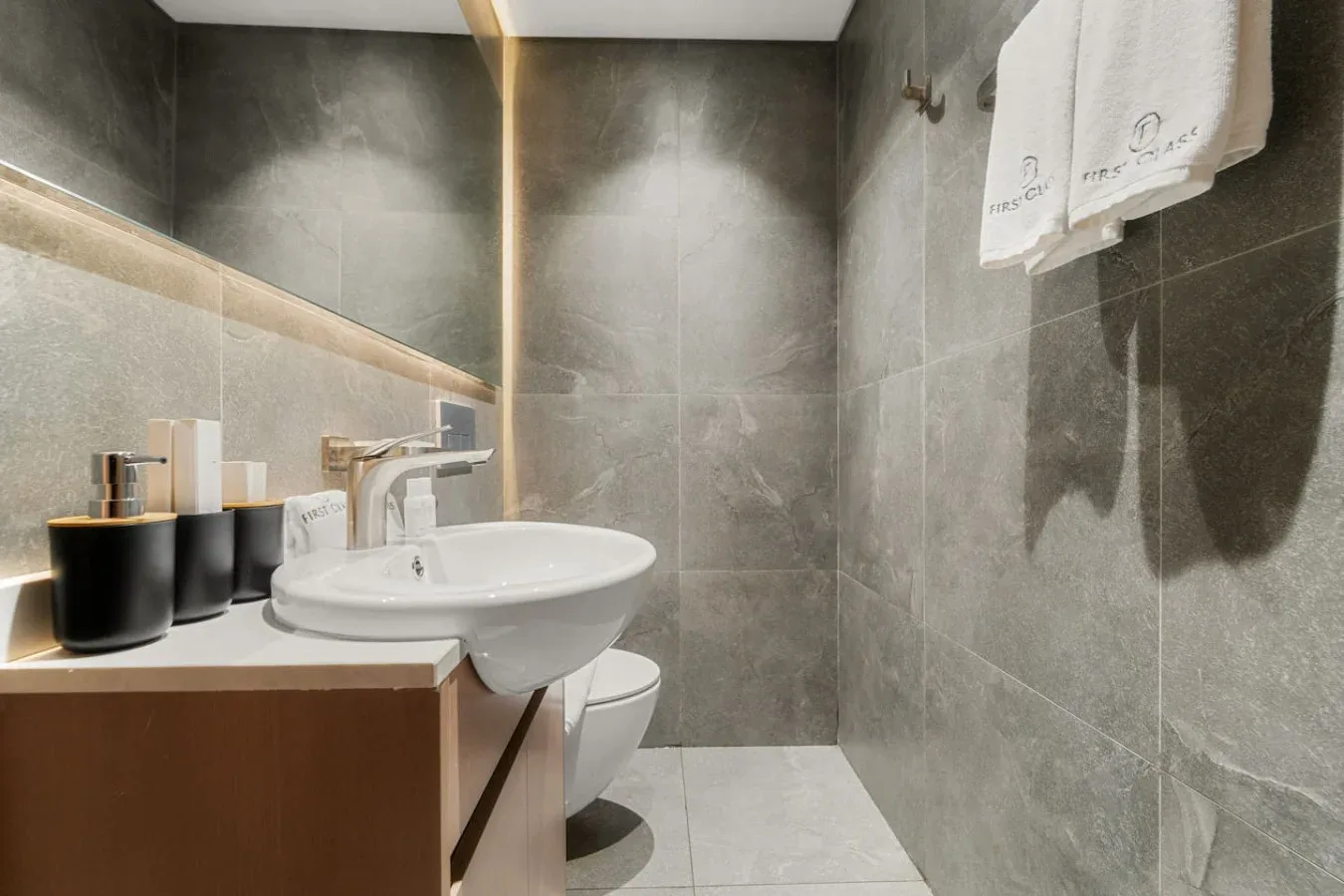 A tiled bathroom with a sink, toilet, and towels hanging on the wall.