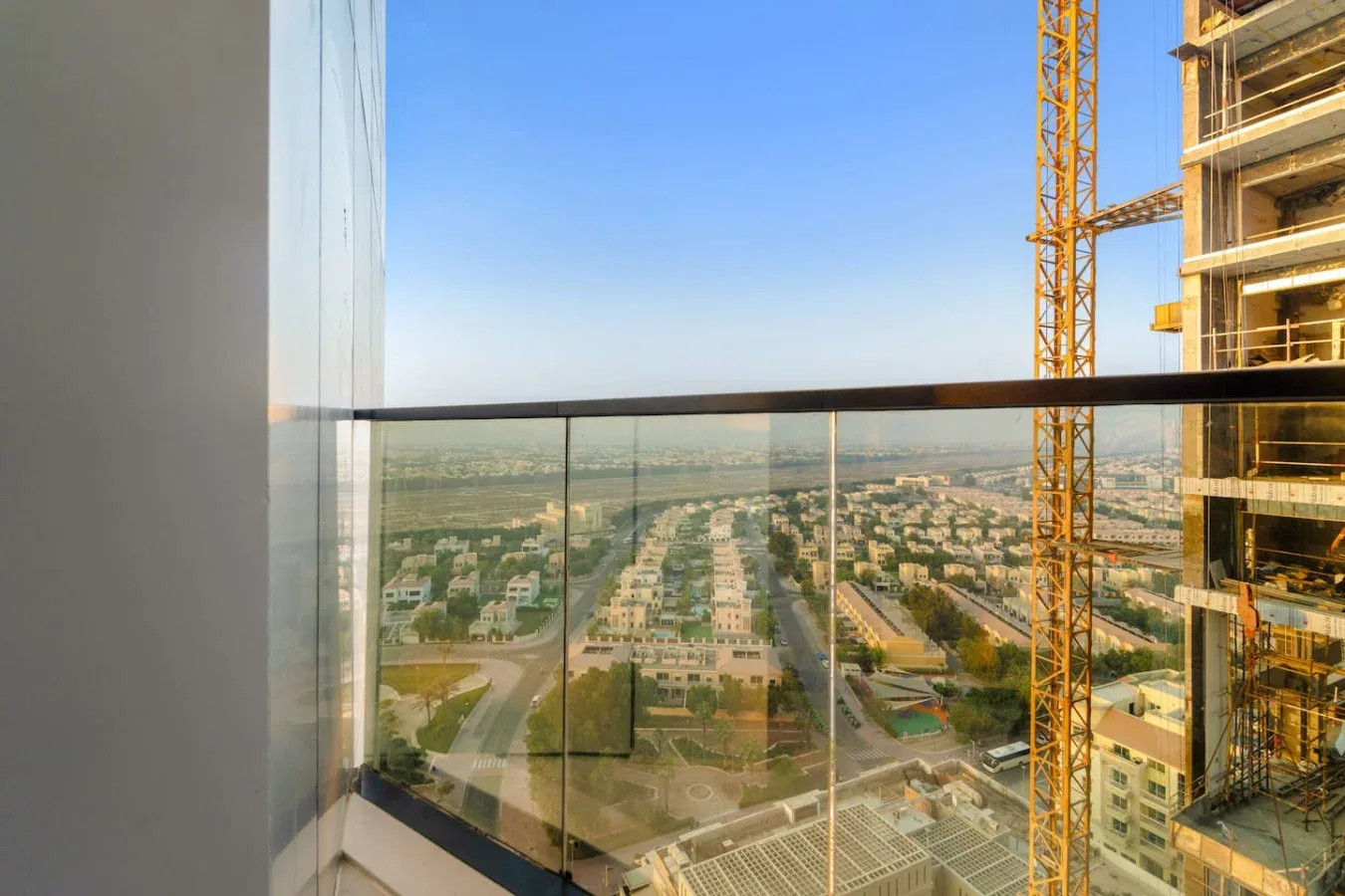 A cityscape viewed from a glass balcony, with a construction crane beside the building.