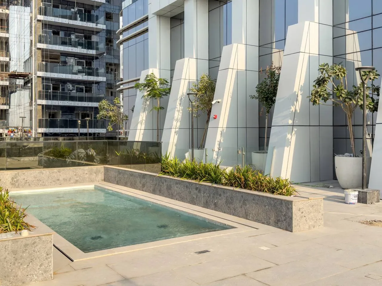 An outdoor courtyard pool sits beside modern buildings and landscaped planters.