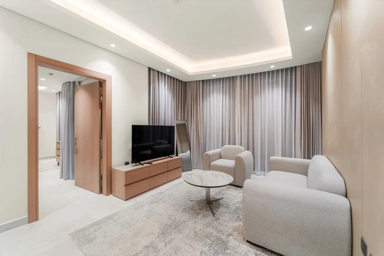 A living room with seating, a television, and floor-to-ceiling curtains.