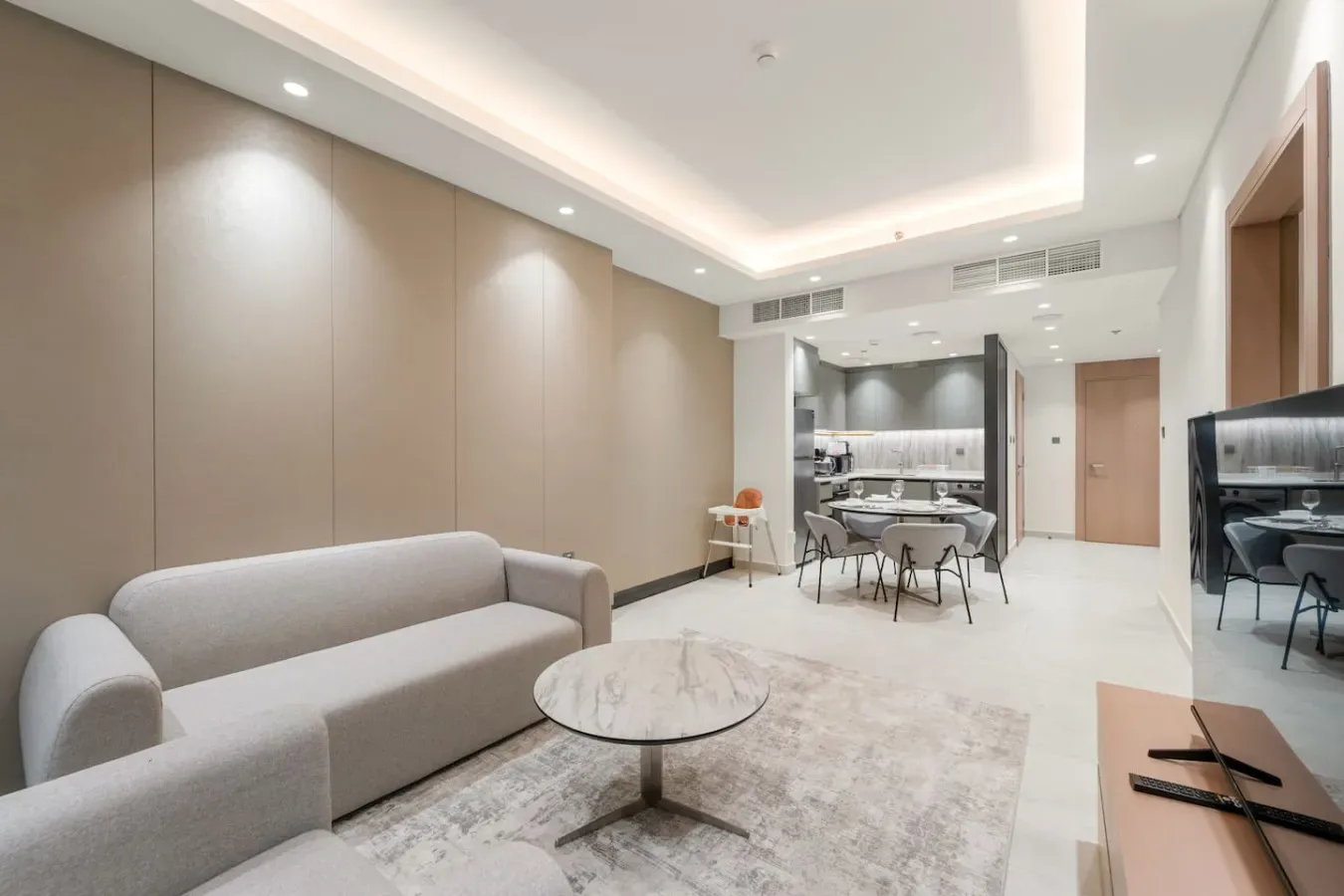 Una sala de estar moderna con sofá claro, mesa de centro y zona de comedor.