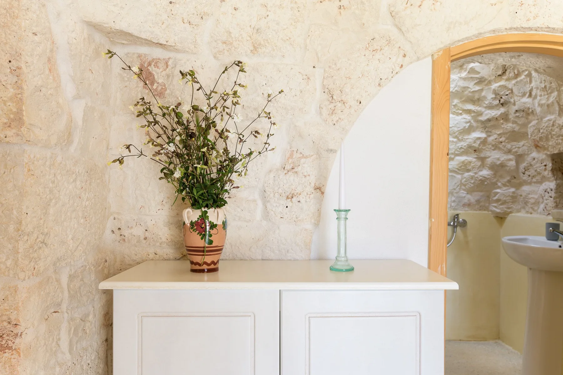 A white console table with a vase stands beside an arched bathroom doorway.