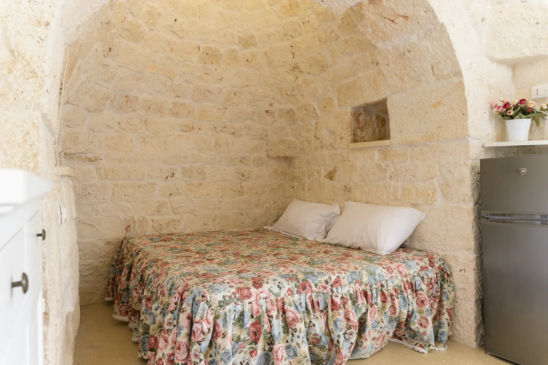 Un dormitorio con una cama cubierta con una colcha floral bajo un arco de piedra.