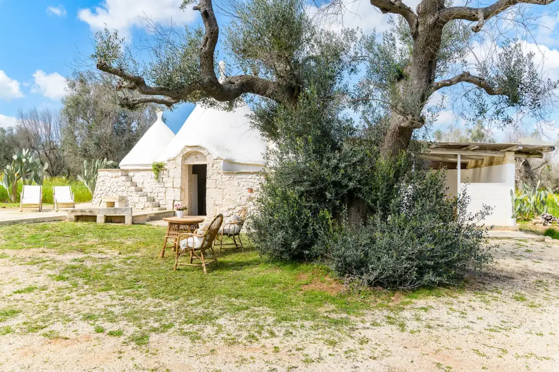 A small stone building with a white roof sits among trees and open lawn.