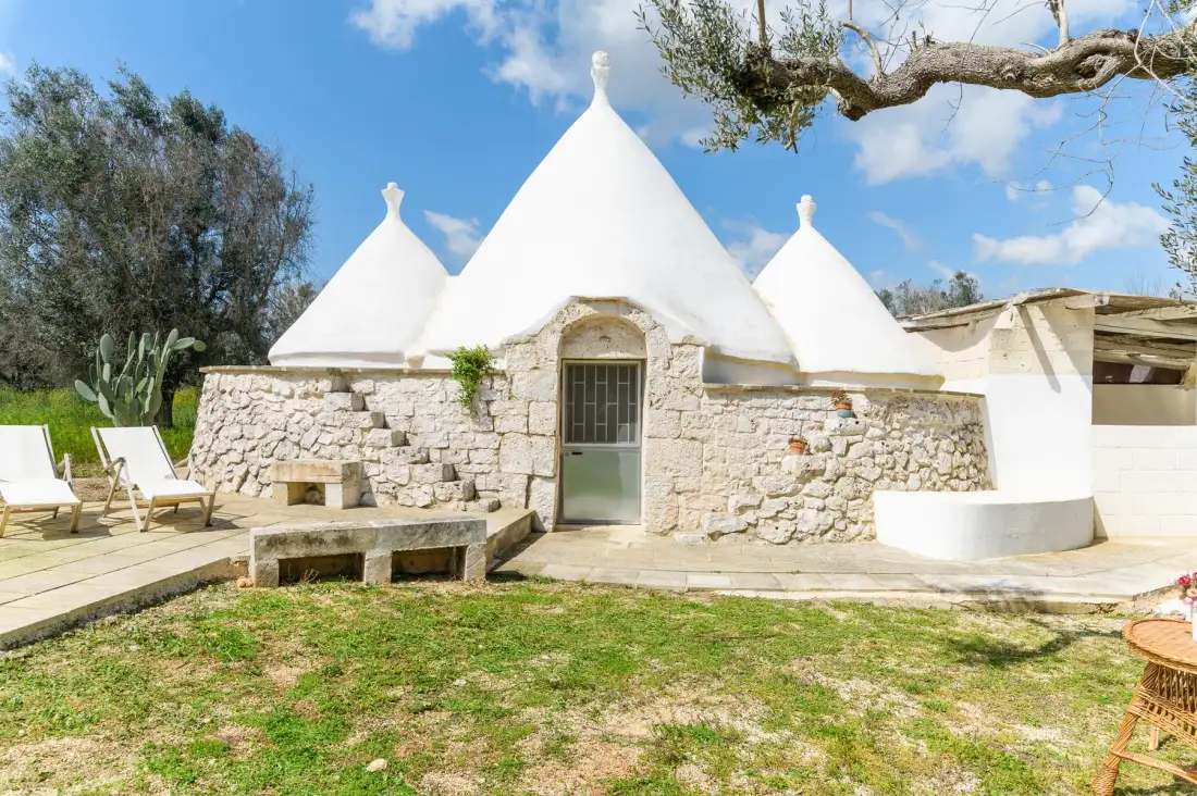 A white stone building with conical roofs stands beside a sunny outdoor patio.