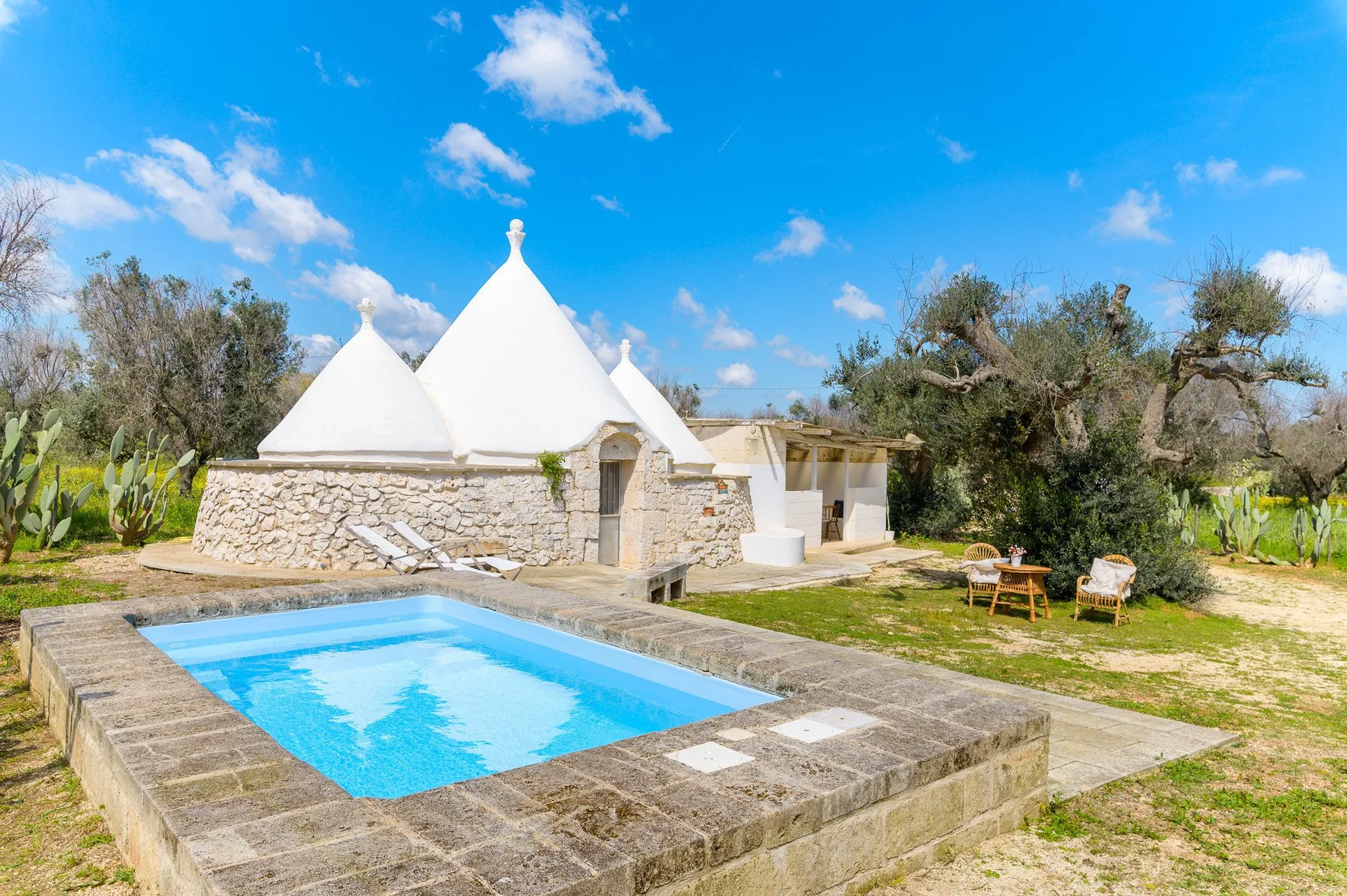 A swimming pool sits beside a white stone building with conical roofs.