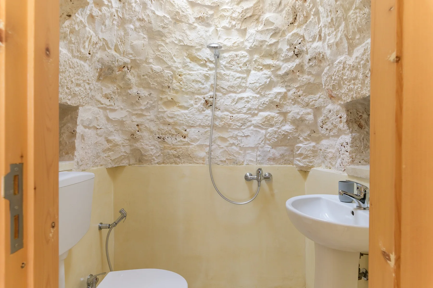 A bathroom with a shower, toilet, and sink against stone walls.