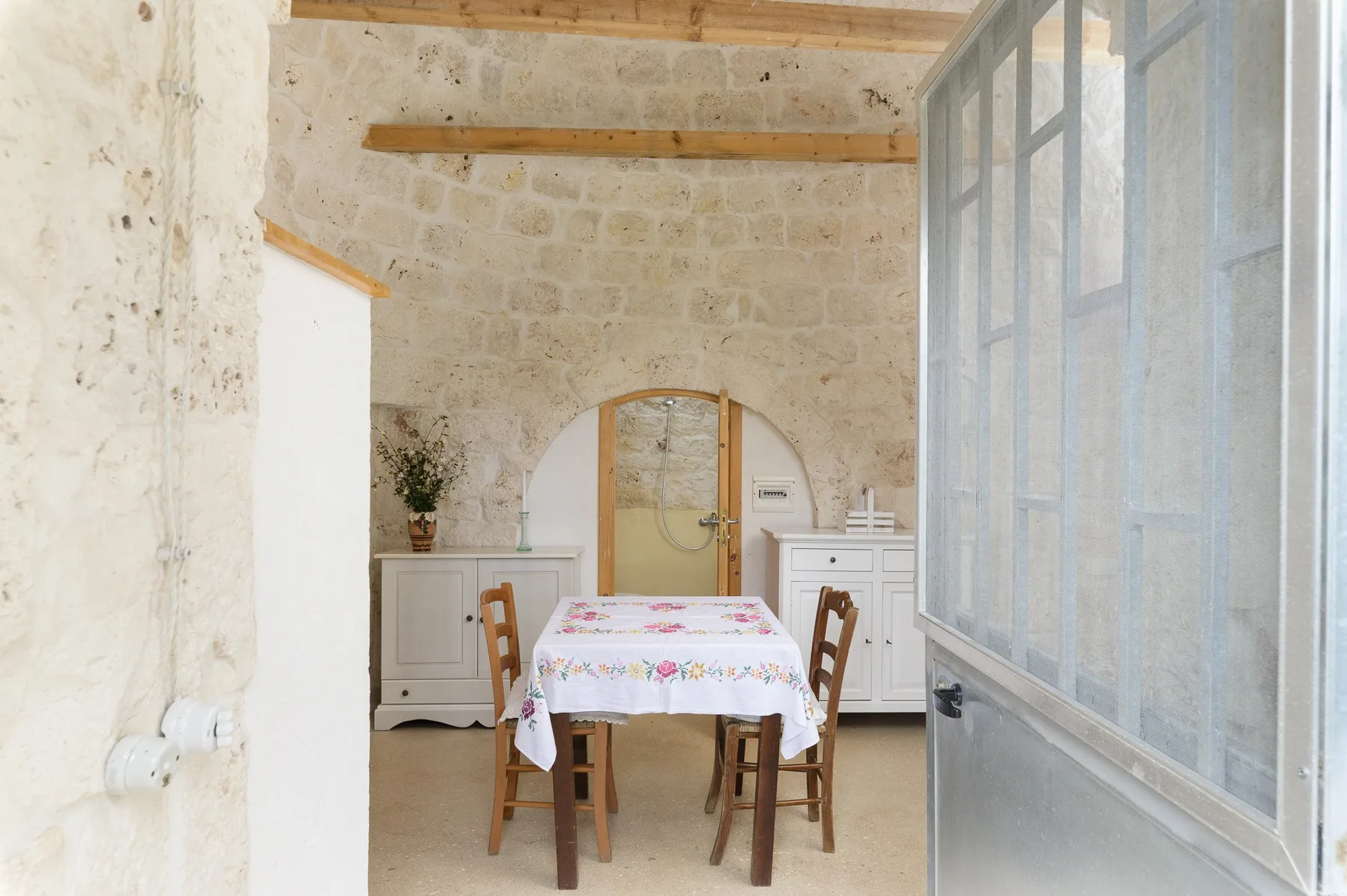 Comedor con mantel floral y asientos de madera junto a una pared de piedra.