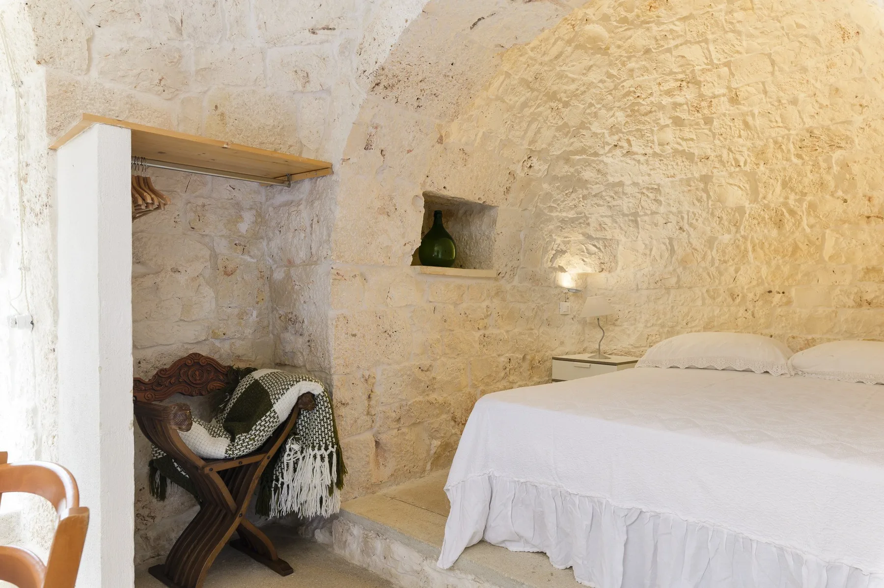 A bedroom with a bed beside a stone wall and a small seating area.