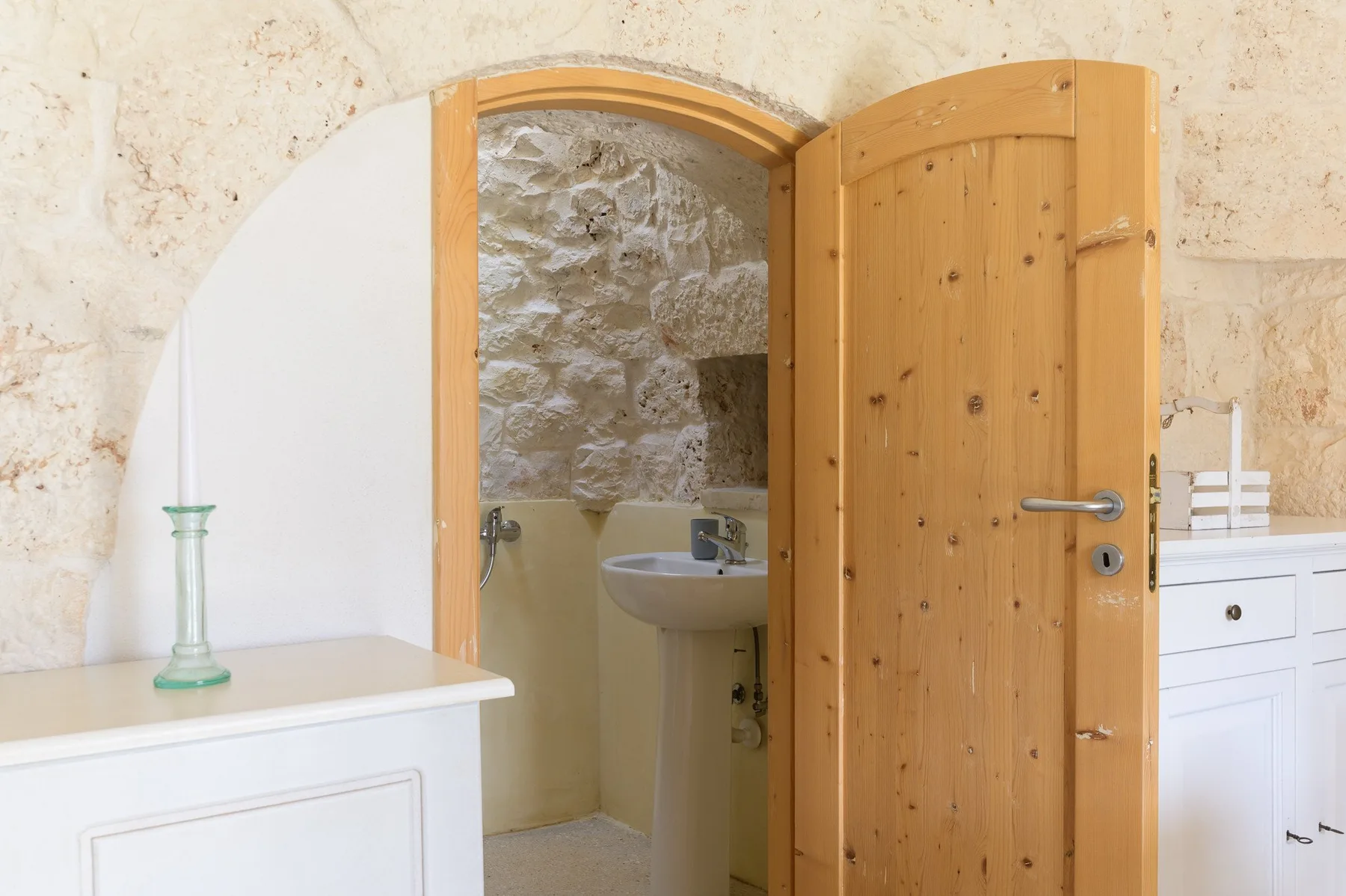 Una puerta da paso a un baño con paredes de piedra y un lavabo.