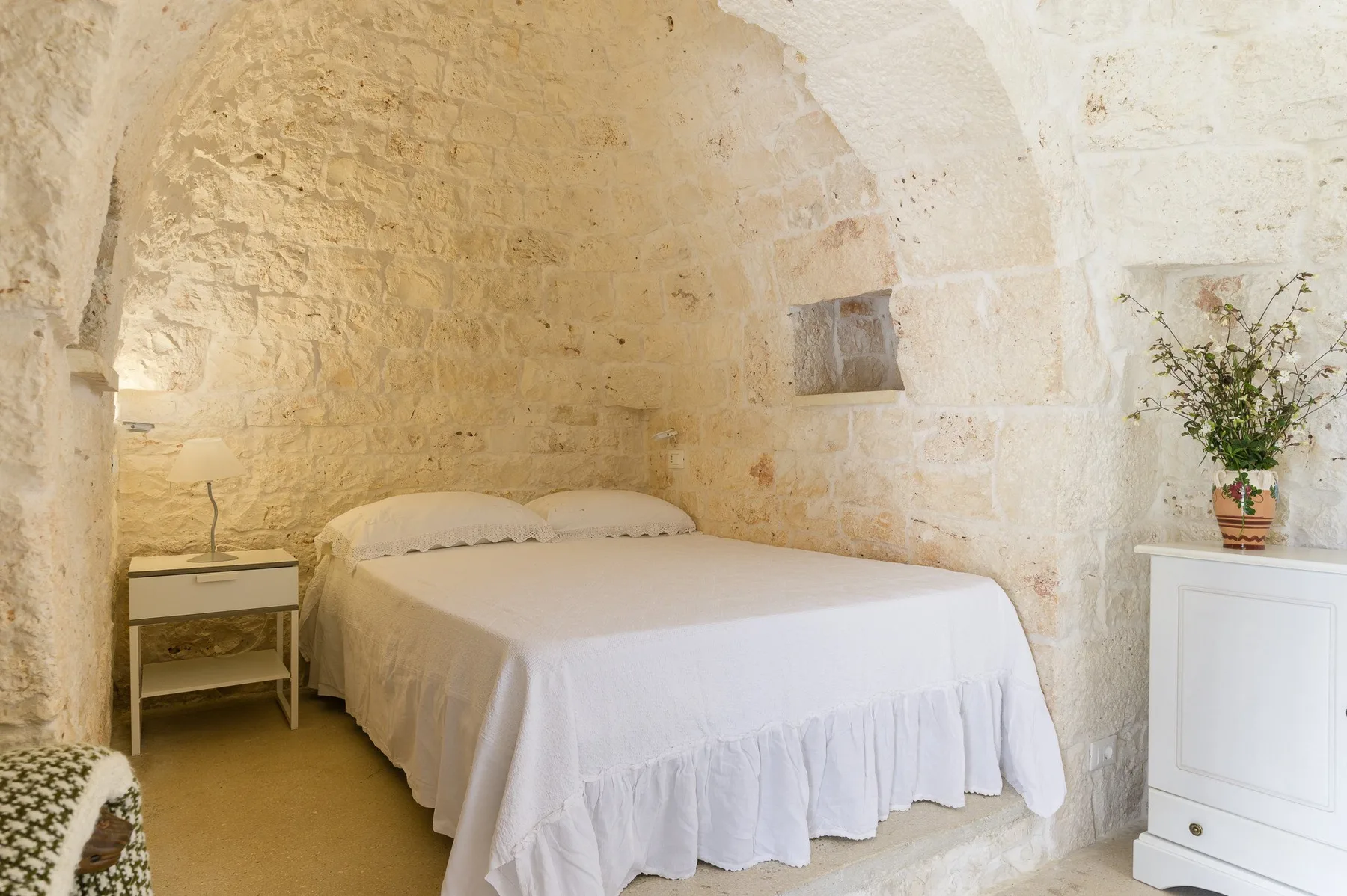 A bedroom with a white bed beneath an arched stone ceiling.