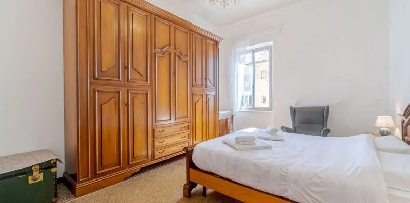 Dormitorio con una cama junto a un gran armario de madera y una ventana.