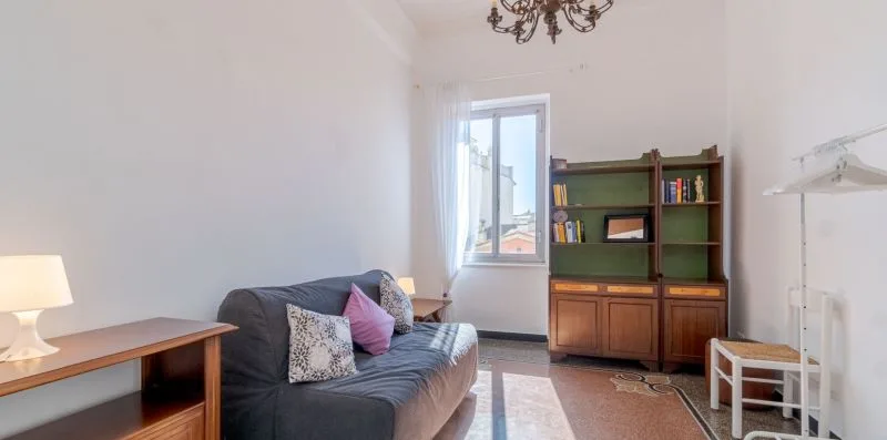 Una sala luminosa con sofá, estantería y ventana.