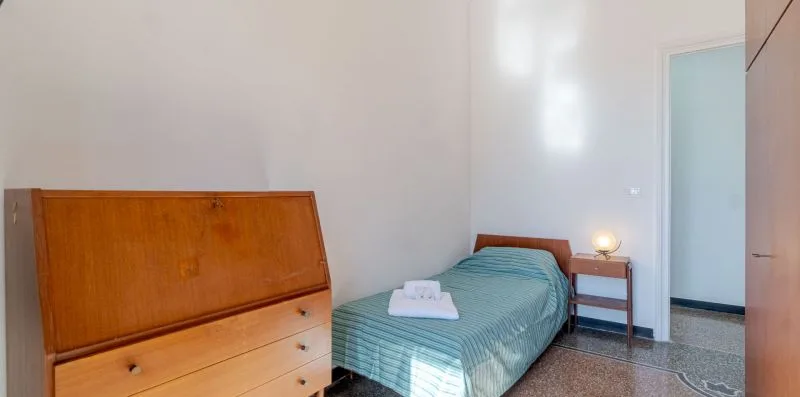 Un dormitorio con una cama individual, una toalla doblada y una cómoda de madera.