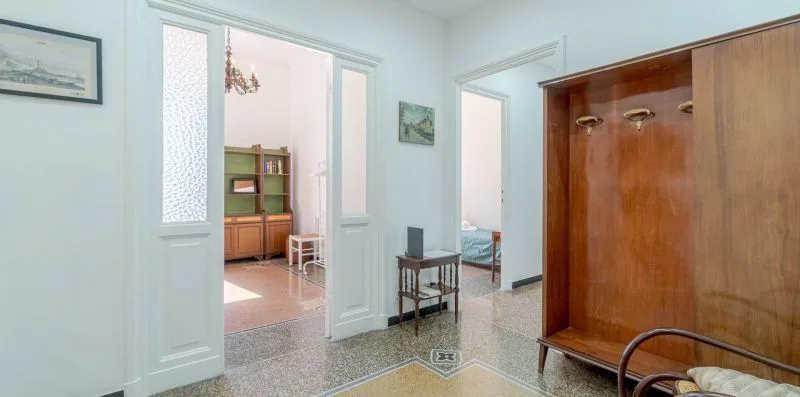A bright interior hallway opens into adjoining rooms, with a wooden coat rack nearby.