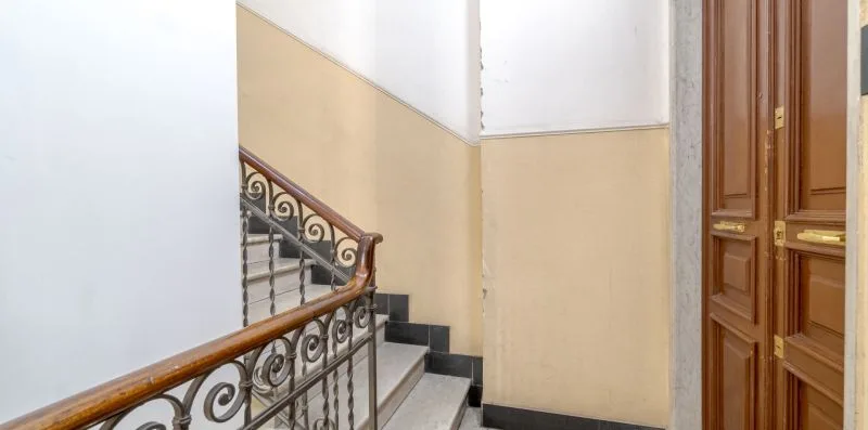 An indoor staircase with ornate metal railing leads up beside paneled wooden doors.