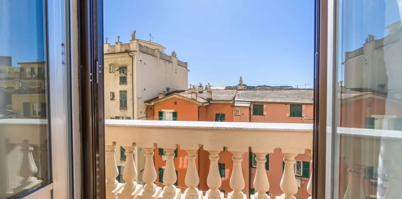 An open window overlooks nearby buildings and a balcony railing.