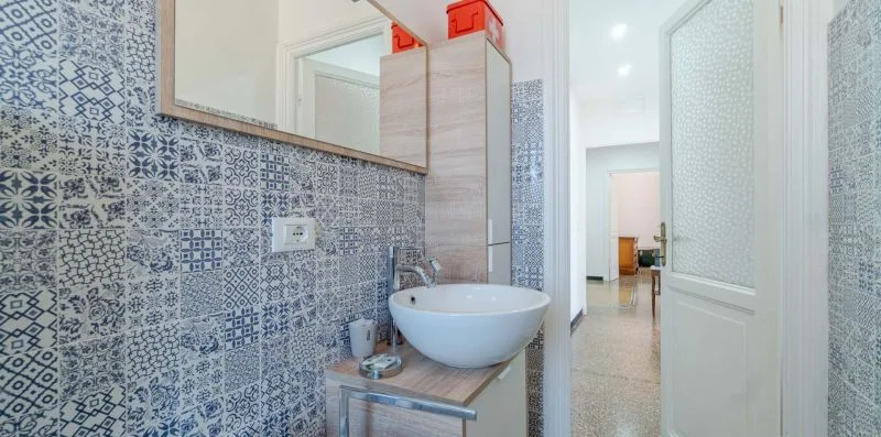 A tiled bathroom with a wall-mounted sink beside an open doorway.