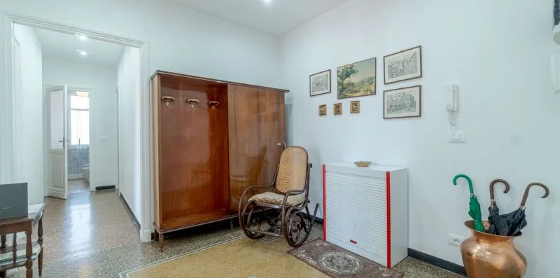 A bright hallway with a wooden wardrobe and a wheelchair beside a radiator.