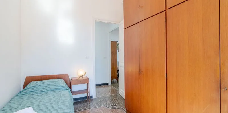 A bedroom with a bed beside a large wooden wardrobe.