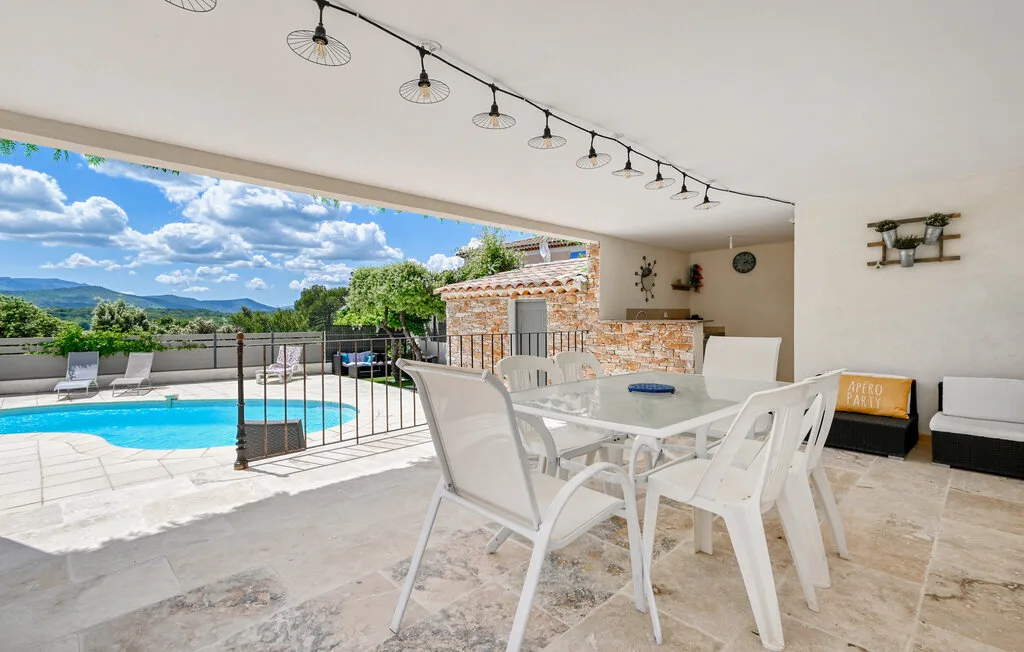 A covered patio dining area opens onto a swimming pool and green hills.