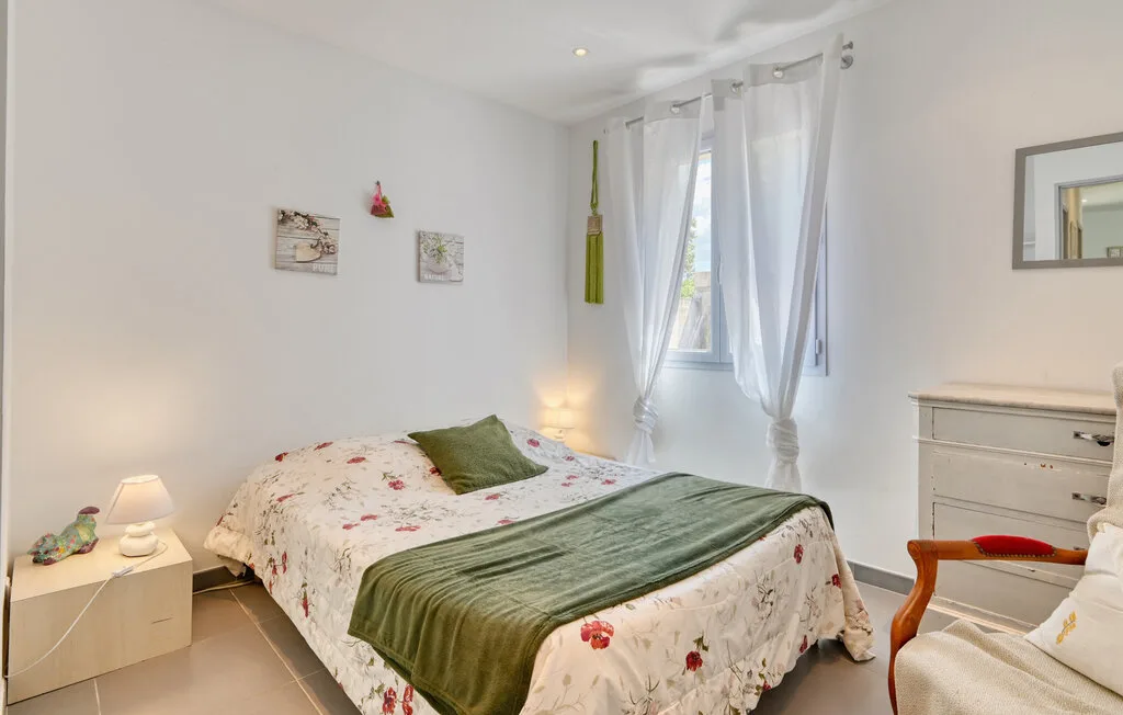 A bright bedroom with a floral bedspread and sheer curtains by the window.