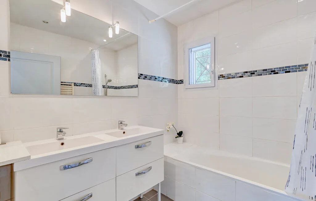 A bright bathroom has a double sink vanity, bathtub, and window.