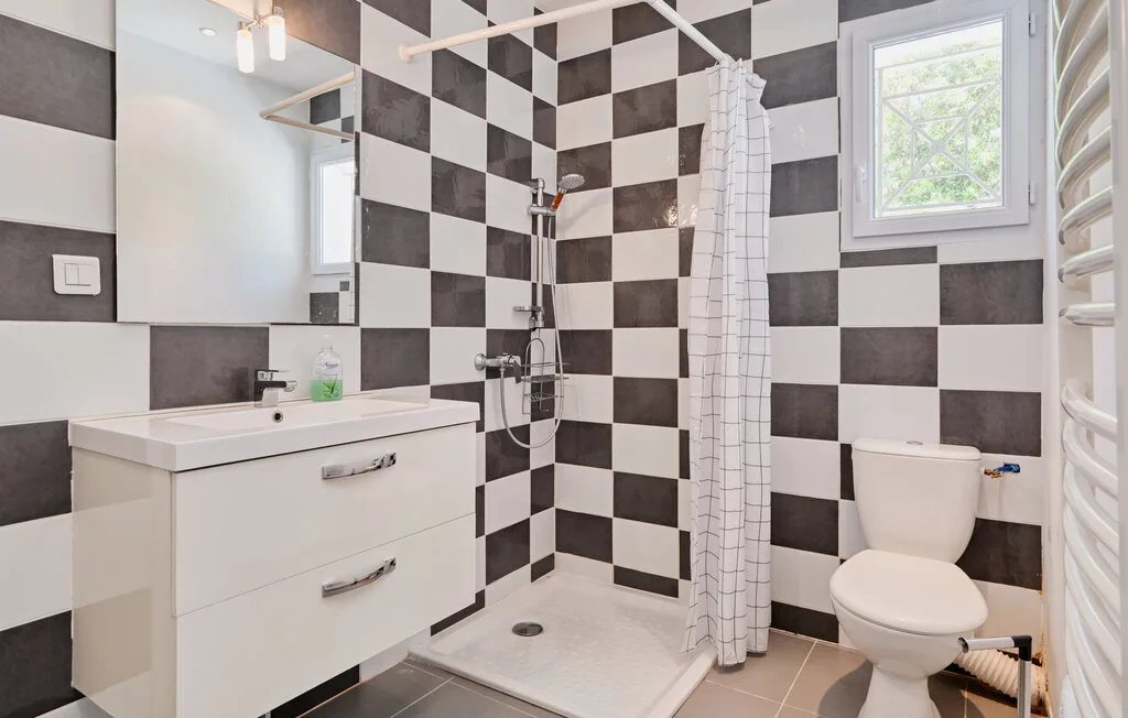 A bathroom with a sink, shower, and black-and-white tiled walls.