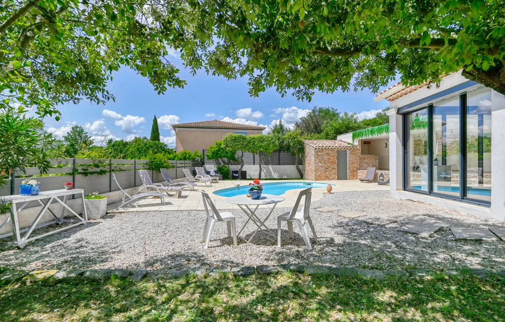 A sunlit outdoor pool area with lounge seating beside a glass-walled building.