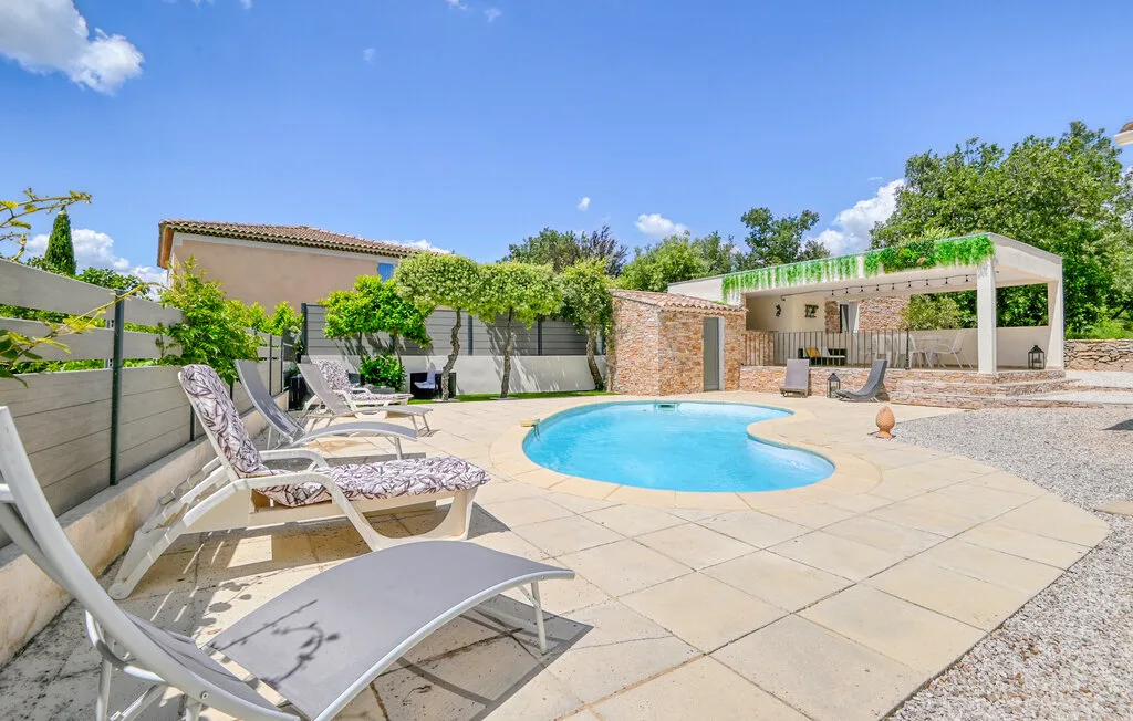 A swimming pool and loungers sit in a sunny paved outdoor courtyard.