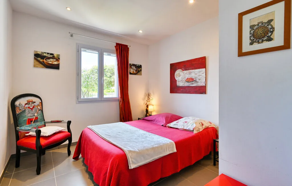 A bedroom with a red-covered bed, a window, and a chair.