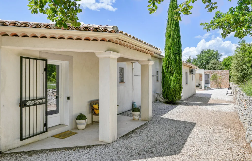 A white building with a covered entrance opens onto a gravel courtyard.