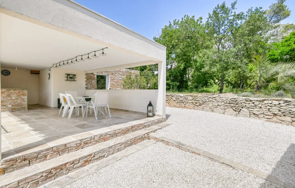 A covered outdoor dining area with white seating opens onto a gravel courtyard.