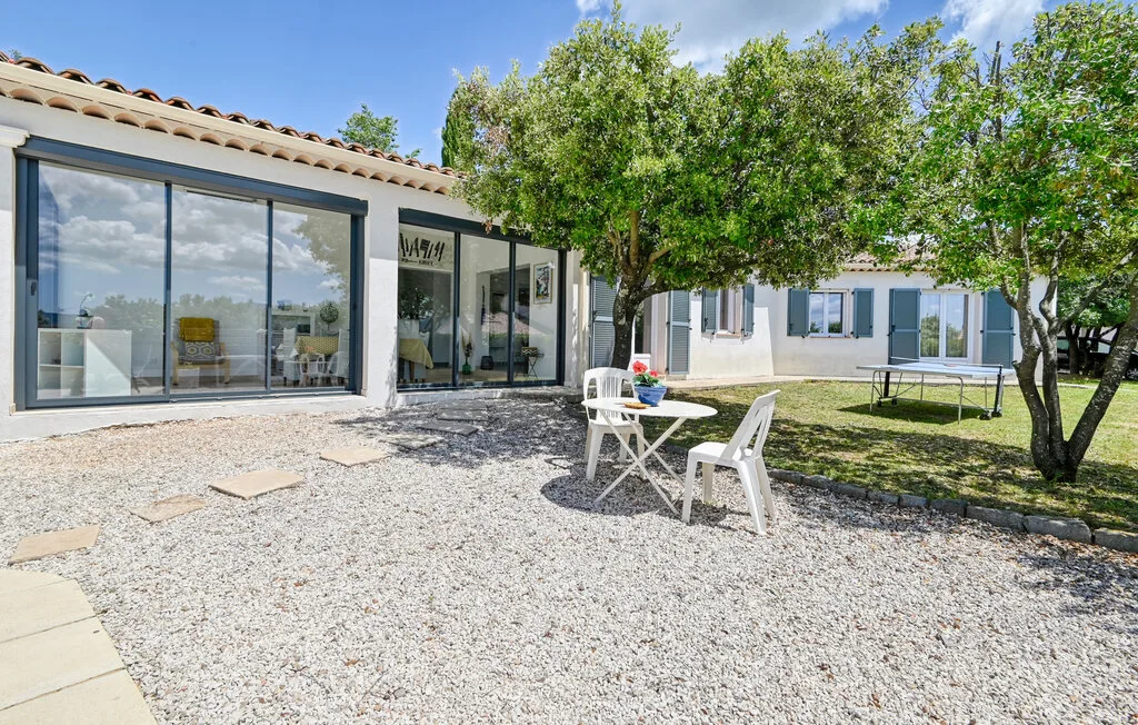 A gravel courtyard with outdoor seating, trees, and glass doors along the house.