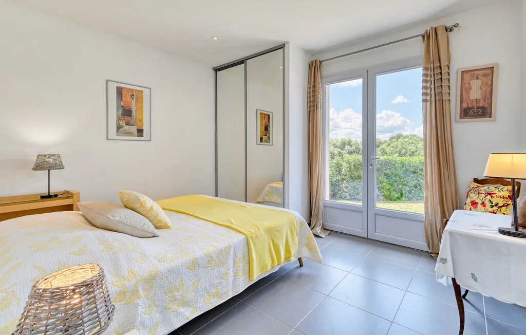 A bright bedroom with a bed beside glass doors and a leafy outdoor view.