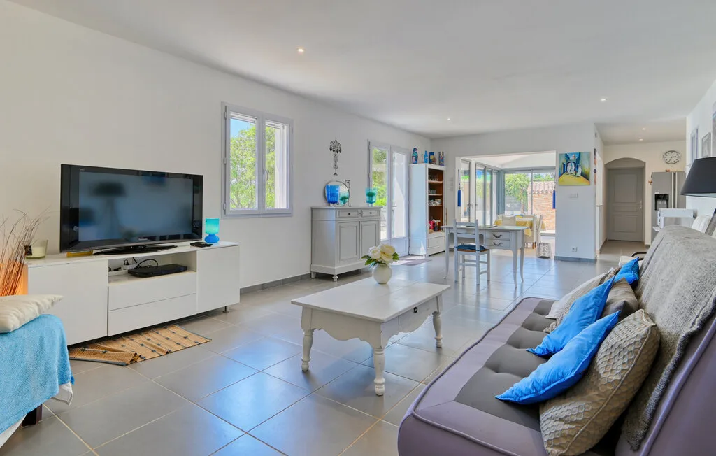 A bright living room with seating, a television, and a dining area beyond.